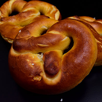 Three golden brown crusted pretzel sprinkled with coarse sea salt/ kosher salt in a black plate.